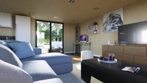 Salon moderne et lumineux dans un module en bois avec grande baie vitrée donnant sur une terrasse extérieure.